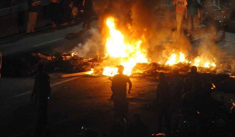 Fogo na BR-381, em Betim, a noite. Homens ao redor dos pneus incendiados.