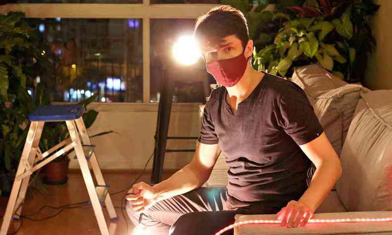 O ator Odilon Esteves, de mscara e camiseta preta, opera cmera na sala de sua casa