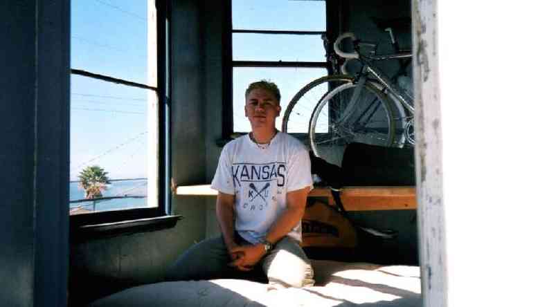 Tom Justice sentado ao lado de uma janela com bicicletas ao fundo