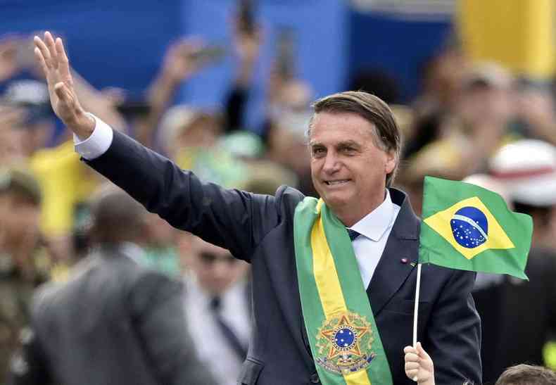 Bolsonaro d 'tchau' para apoiadores e segura bandeira do Brasil
