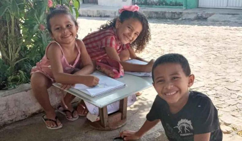 Trs crianas, sorrindo, com cadernos na mo.