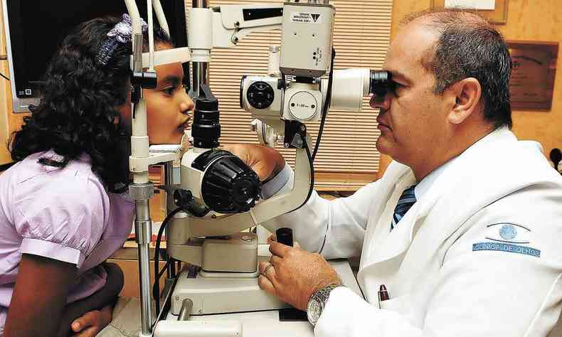 Olhos de menina so examinados por mdico por meio de equipamento oftalmolgico 