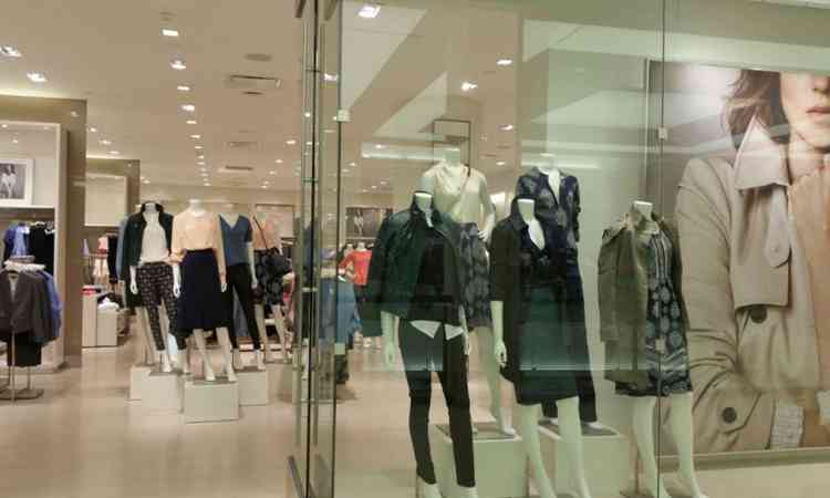 loja de roupas; na vitrine estão três manequins bem vestidos com casacos