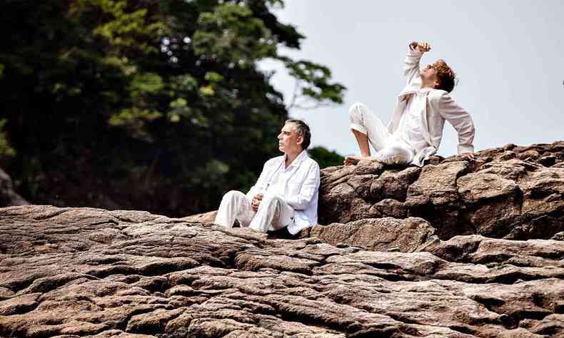 vestidos de branco, sentados em formao rochosa, Arnaldo Antunes e Vitor Araujo observam o sol 