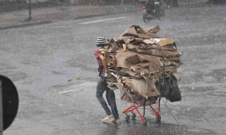 Catador atravessa rua com carrinho na chuva 