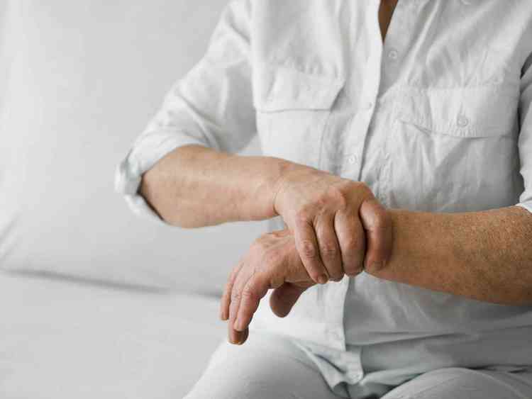 Pessoa parda de blusa branca segurando o pulso