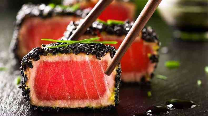 Maki roll de atum com crosta de gergelim sendo pego por um hashi