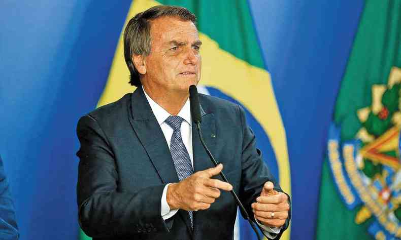 Bolsonaro discursa ao microfone; ao fundo, uma bandeira do Brasil
