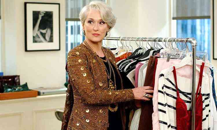 Meryl Street, de casaco dourado, mexe em arara de roupas e olha para trs em cena do filme O diabo veste Prada