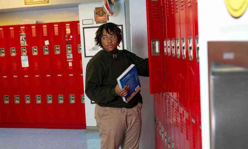 Um homem trans negro de p em frente a armrios, segurando um livro