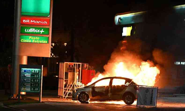 Carro pegando fogo em frente a um posto de gasolina  noite