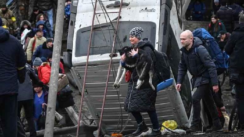 Uma mulher carrega um cachorro enquanto as pessoas atravessam uma ponte destruda na cidade de Irpin, a noroeste de Kiev, 5 de maro de 2022
