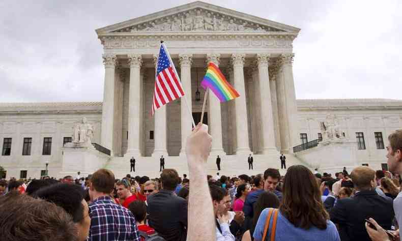 Imagem externa da Suprema Corte dos EUA.  frente da construo, uma mo branca levanta as bandeiras dos EUA e do movimento LGBTQIA+