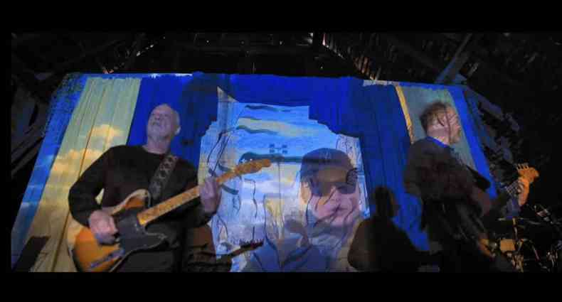Msicos tocando, ao fundo imagens da bandeira ucraniana e do artista Andriy Khlyvnyuk em um projetor.