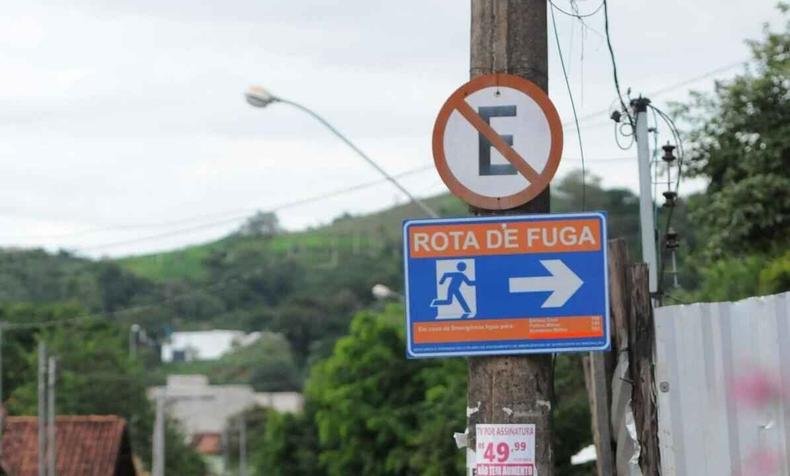 Placa escrito 'Rota de Fuga' e seta apontando para a direita. Acima, placa de proibido estacionar. 
