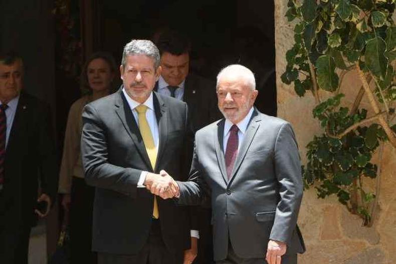 Arthur Lira e Lula fazem aperto de mos enquanto olham para a foto