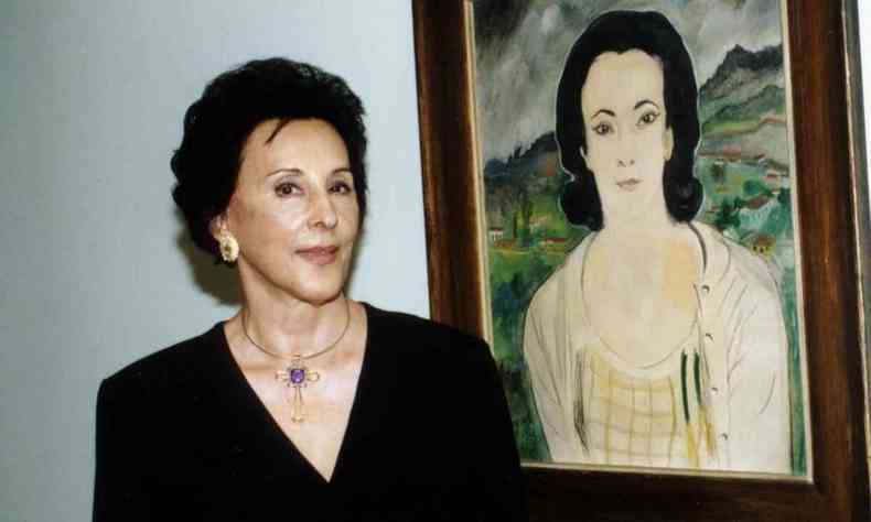 Heloisa Aleixo Lustosa, ex-diretora do Museu de Arte Moderna do Rio, ao lado do quadro com o retrato pintado dela
