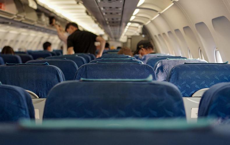 Interior de avio visto do fundo. Um passageiro aparece em p, alguns esto sentando, mas boa parte do avio est vazio. 