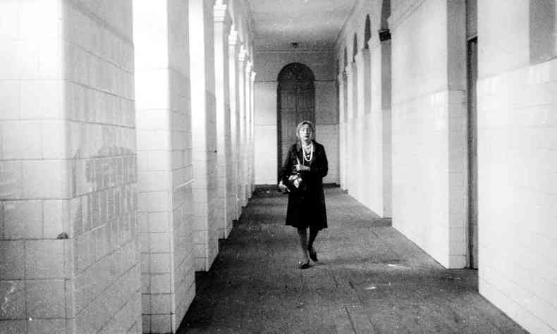 De vestido e colar, Clarice Lispector caminha sozinha por um extenso corredor