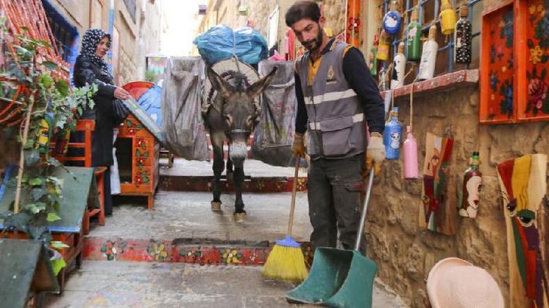 Os burros são usados até hoje para tarefas surpreendentes, como limpar as ruas estreitas da cidade de Mardin, na Turquia(foto: Anadolu Agency) Um funcionário da limpeza municipal limpa as ruas %u2014 e atrás dele um burro carrega os sacos de lixo