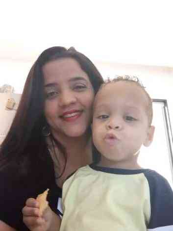 Selfie de Emilena, mulher branca com cabelos pretos longos junto de seu filho Heitor de Seis anos, branco que est comendo um salgadinho