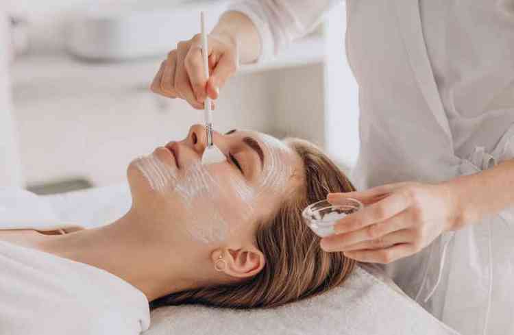 Cosmetologista fazendo tratamento facial e aplicando mscara facial