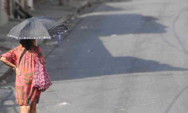 Imagem de uma mulher andando com uma sombrinha sob o asfalto quente