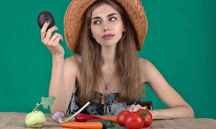 mulher com várias opções de legumes e verduras em sua frente, em cima de uma mesa