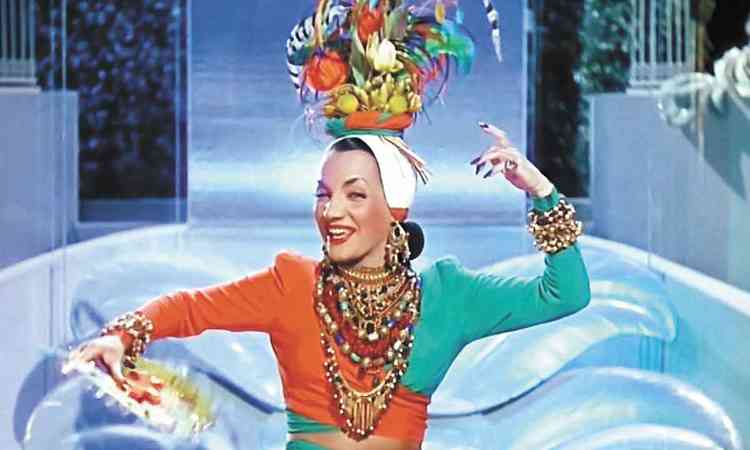 De vestido multicolorido e acessrio na cabea, Carmen Miranda pisca e sorri em cena de Aconteceu em Havana
