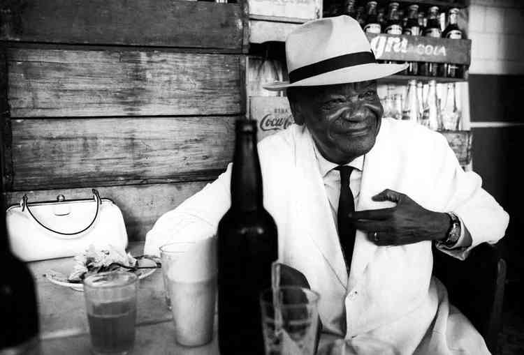 Compositor Pixinguinha, de terno branco e chapu, sentado em bar carioca