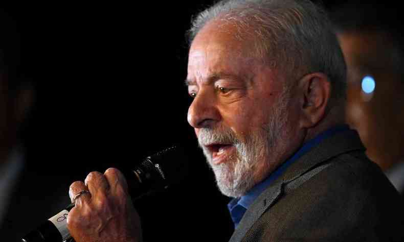 Lula falando ao microfone. Ele  um homem branco, de cabelo e barba branca e veste um terno cinza escuro