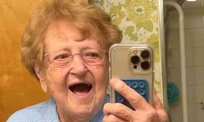 Lilian Droniak, uma senhora de 93 anos, sorrindo enquanto tira uma foto em frente ao espelho do banheiro