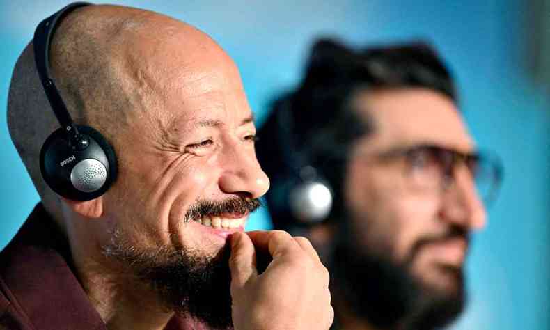 Usando fones de ouvido, diretor Tarik Saleh sorri, com a mão no queixo, durante entrevista no Festival de Cannes 
