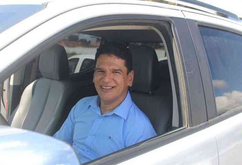prefeito, de camisa social azul, est sorrindo dentro de um carro branco
