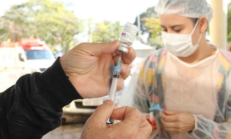 Seringa de vacina contra a COVID-19, e enfermeira ao fundo da foto
