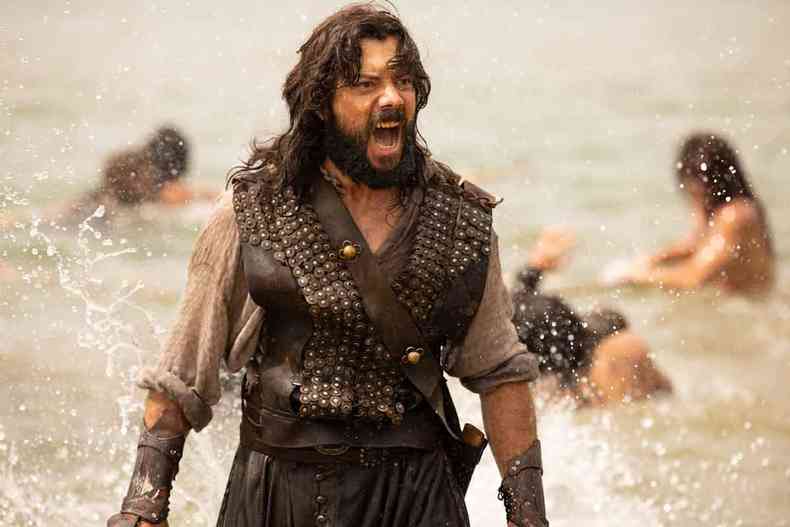 O ator Álvaro Morte, à beira do mar, como o personagem Elcano, gritaem cena de Sem Limites