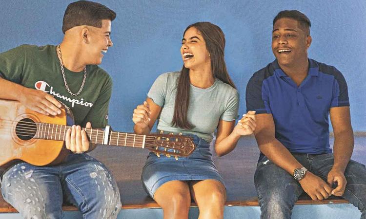 Os atores Jottap, Bruna Mascarenhas e Christian Malheiros, sentados em mureta, sorriem, em cena de 'Sintonia' 