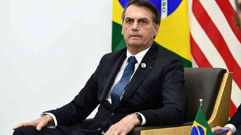 Bolsonaro sentado em cadeira com bandeiras do Brasil e de outro pas atrs