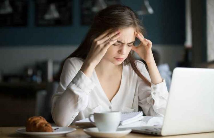 Aluna sentindo dor de cabeça estudando no café