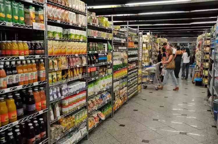 Prateleiras de um supermercado; consumidores circulam com carrinhos e compras