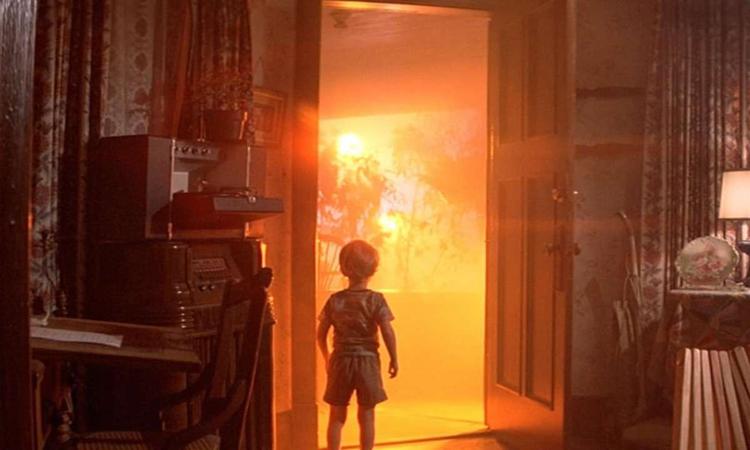 Criana em frente a porta aberta, de onde se v intensa luz amarela em cena do filme Contatos imediatos de terceiro grau
