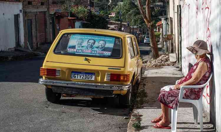 Foto do bairro Palmital mostra senhora sentada em cadeira, na rua, e carro Braslia estacionado com cartazes de polticos em campanha
