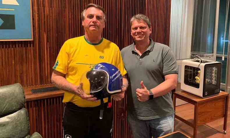 Bolsonaro segurando um capacete, vestindo uma camiseta amarela, ao lado de Tarcsio que veste camiseta cinza