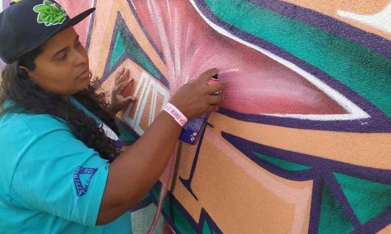 De bon, Tina faz grafite numa parede, com as cores laranja, roxo e verde