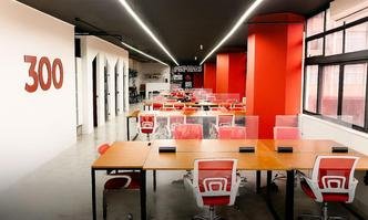 Cadeiras vermelhas em mesas de madeira com colunas vermelhas e teto preto, indicando um escrit�rio moderno.