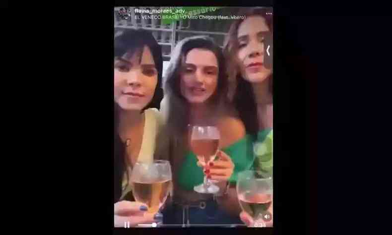 Foto tirada do vídeo mostra advogada entre duas mulheres; as três tên taças de bebida nas mãos