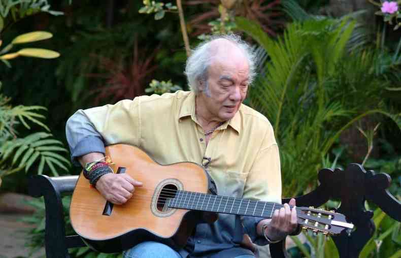 Cantor e compositor Erasmo Carlos, de camisa amarela e cinza, toca violo em meio a um jardim