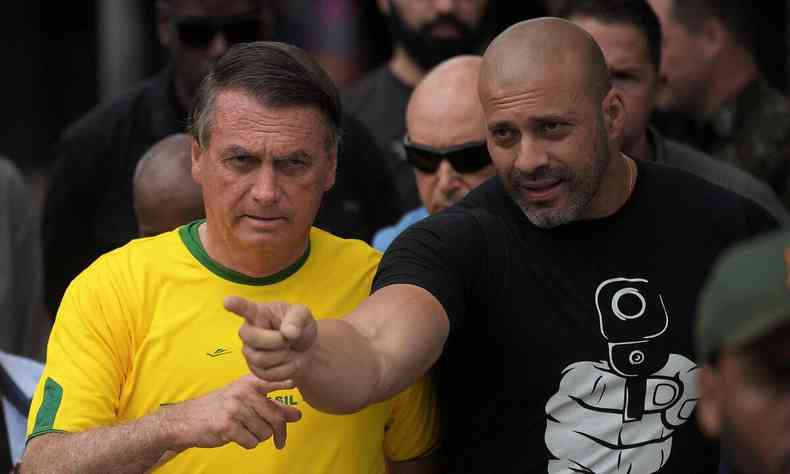 Daniel Silveira (PTB-RJ) com uma camisa em que uma mo segura uma arma, ao lado do ento presidente Jair Bolsonaro (PL) de camisa amarela