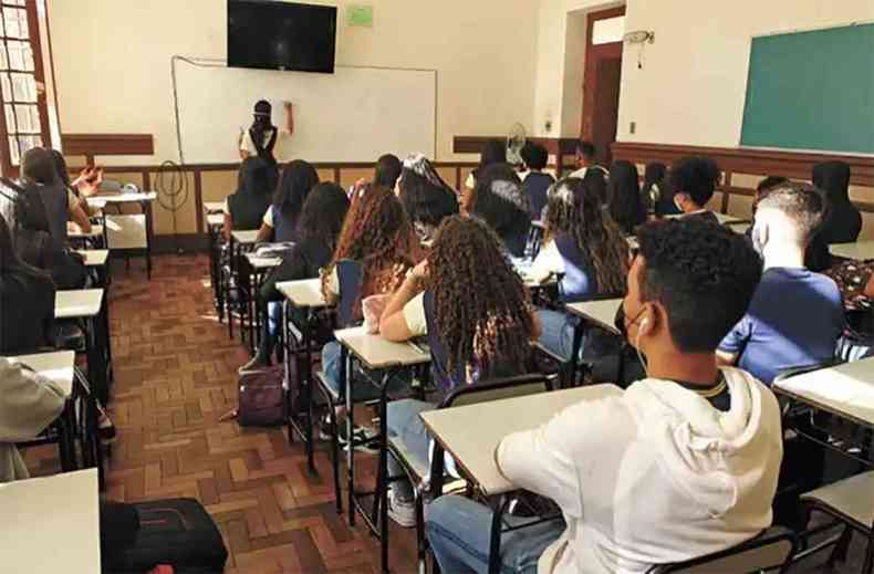 Escola Dom Pedro II em Belo Horizonte alunos sentados assistem professora escrever no quadro durante aula
