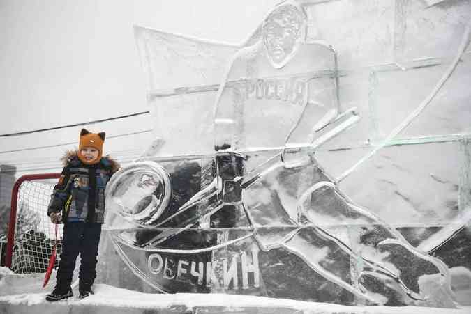 Menino bem agasalhado posa em frente a escultura gelada do astro do hquei Alexander Ovechkin Alexander NEMENOV / AFP